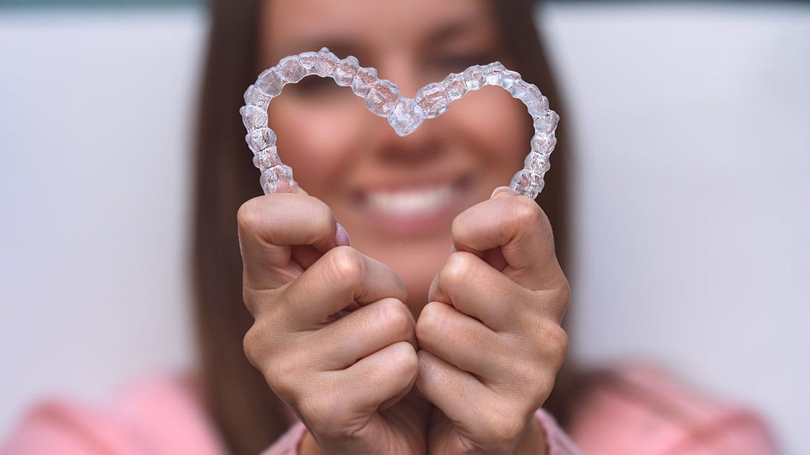 Patient holding Invisalign clear aligners in a heart shape at Beyazada Dental Clinic in Antalya.